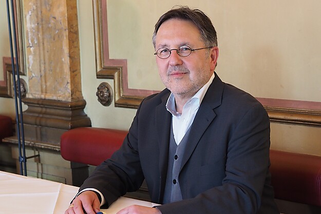 Mann mit Brille in dunklem Anzug sitzt an einem Schreibtisch